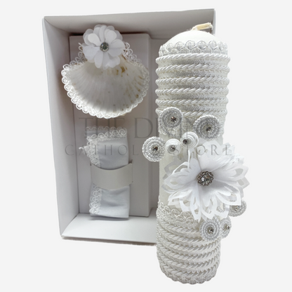 The image features a beautifully designed 3-piece baptism candle set, including a candle, a towel, and a shell. The candle is adorned with white fabric, a braided nylon rope design, small white flowers, and rhinestone embellishments, giving it an elegant and sacred look. The towel and shell complement the set, creating a cohesive design perfect for a baptism ceremony.