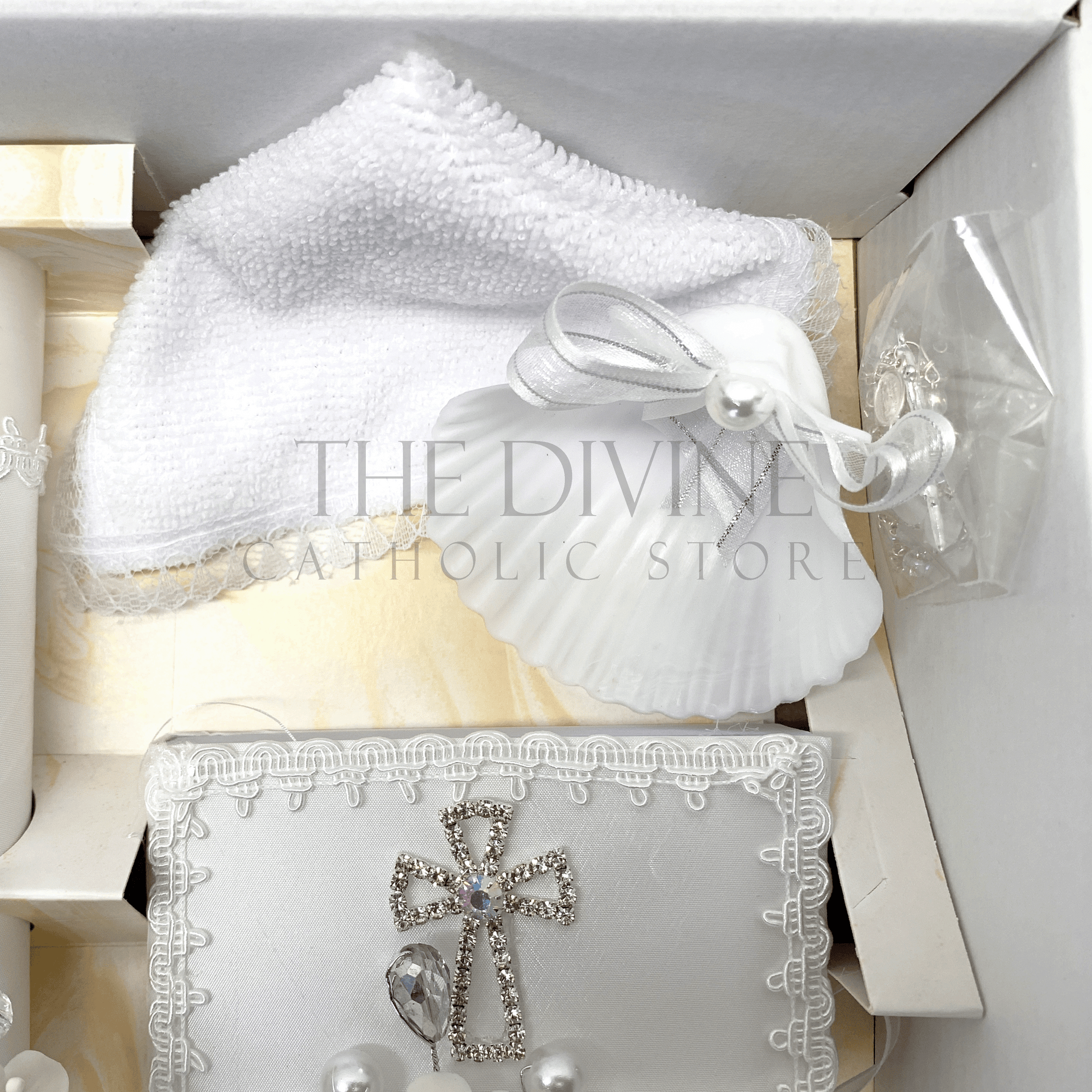 Close up image of the 5 piece baptism candle set showing white candle, shell with white ribbon and white pearl bead, white crystal beaded rosary, and bible covered in fabric with nylon thread bordered with crystal rhinestone cross.