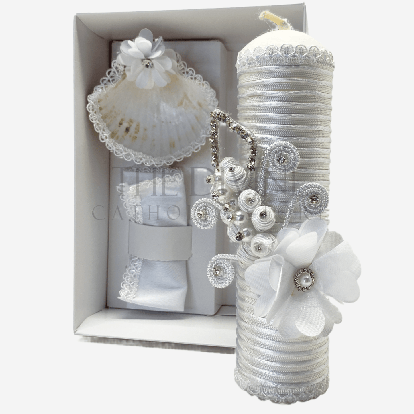 The image features a beautifully designed 3-piece baptism candle set, including a candle, a towel, and a shell. The candle is adorned with white fabric, a braided nylon rope, small white flowers, and rhinestone embellishments, giving it an elegant and sacred look. The towel and shell complement the set, creating a cohesive design perfect for a baptism ceremony.