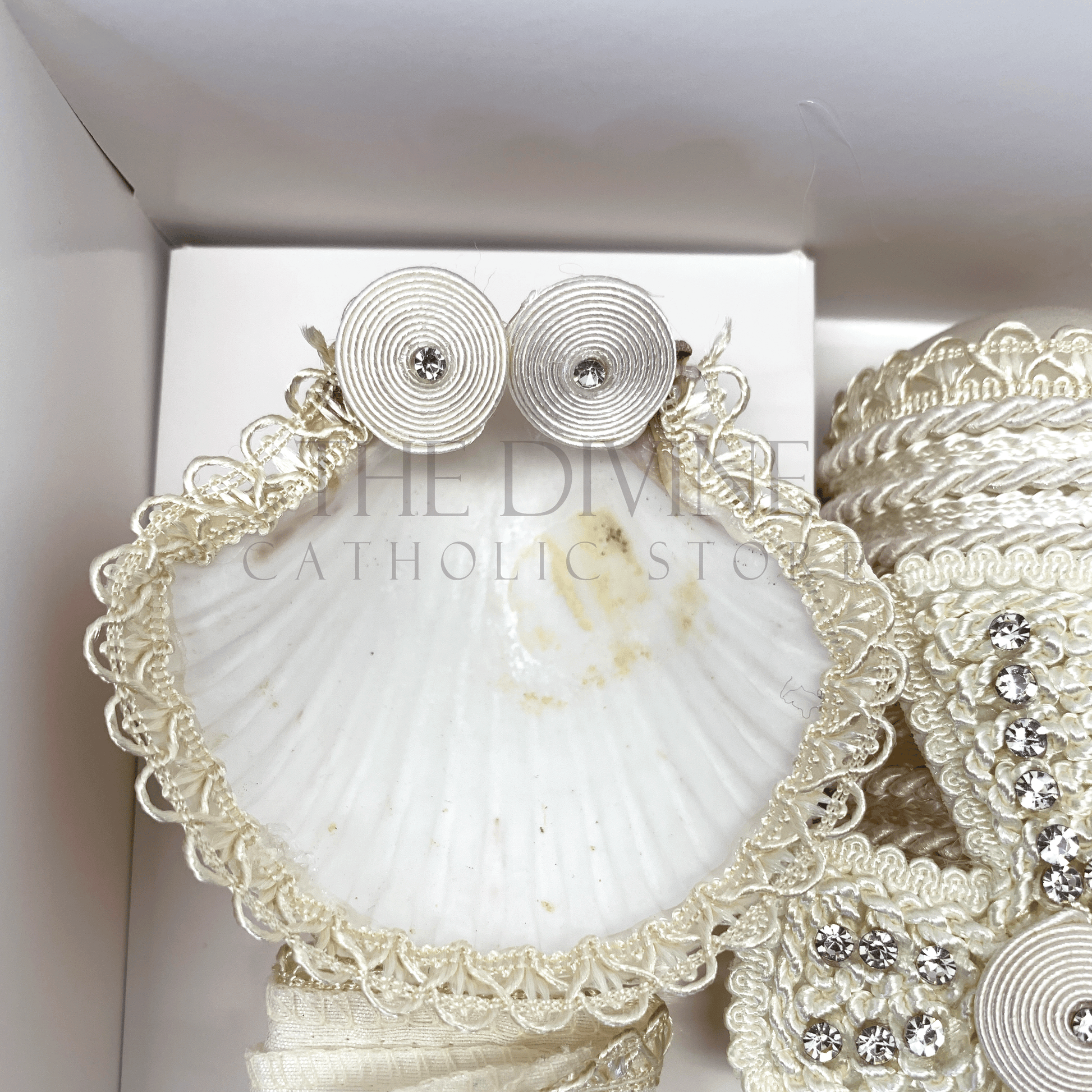 Close up image of the 3 piece baptism candle set shell, embroidered in white nylon thread, and white flower with white bead and rhinestone.