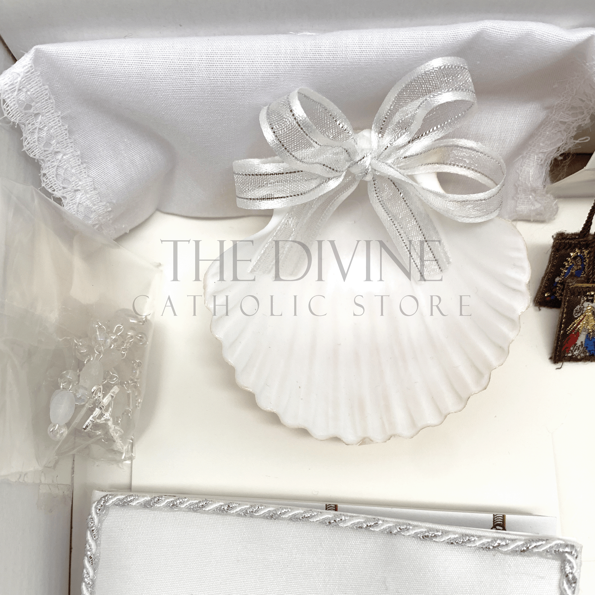 Close up image of the 6 piece baptism candle set showing white candle, shell with white ribbon, white crystal beaded rosary, and bible covered in fabric with nylon thread embroidered, and scapular with Divine Mercy and Our Lady of Guadalupe image, and fabric towel. 