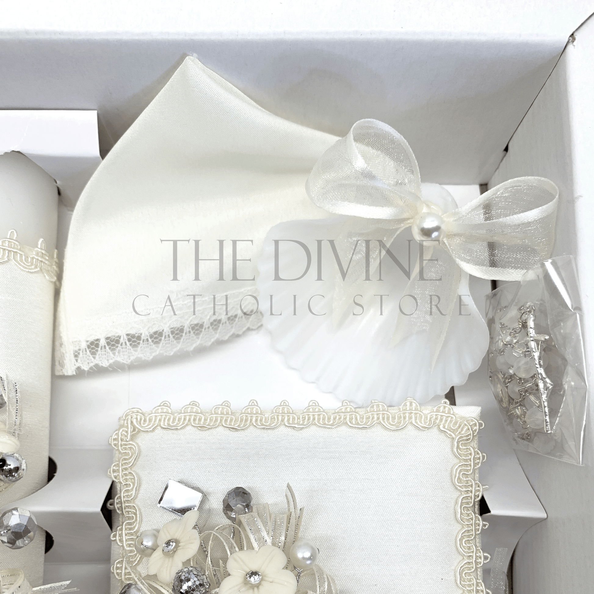 Close up image of the 5 piece baptism candle set showing white candle, shell with white ribbon and white pearl bead, white crystal beaded rosary, and bible covered in fabric with embroidered nylon thread , rhinestones, mirror pieces, pearl beads and ribbon.