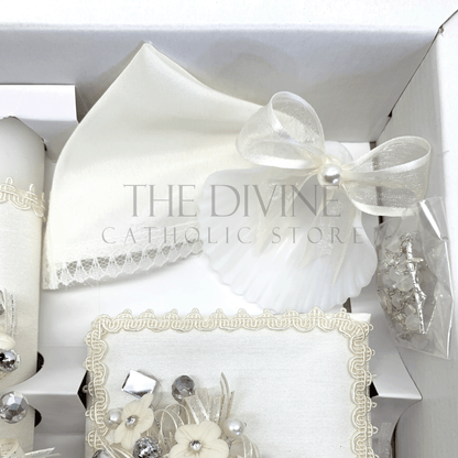 Close up image of the 5 piece baptism candle set showing white candle, shell with white ribbon and white pearl bead, white crystal beaded rosary, and bible covered in fabric with embroidered nylon thread , rhinestones, mirror pieces, pearl beads and ribbon.